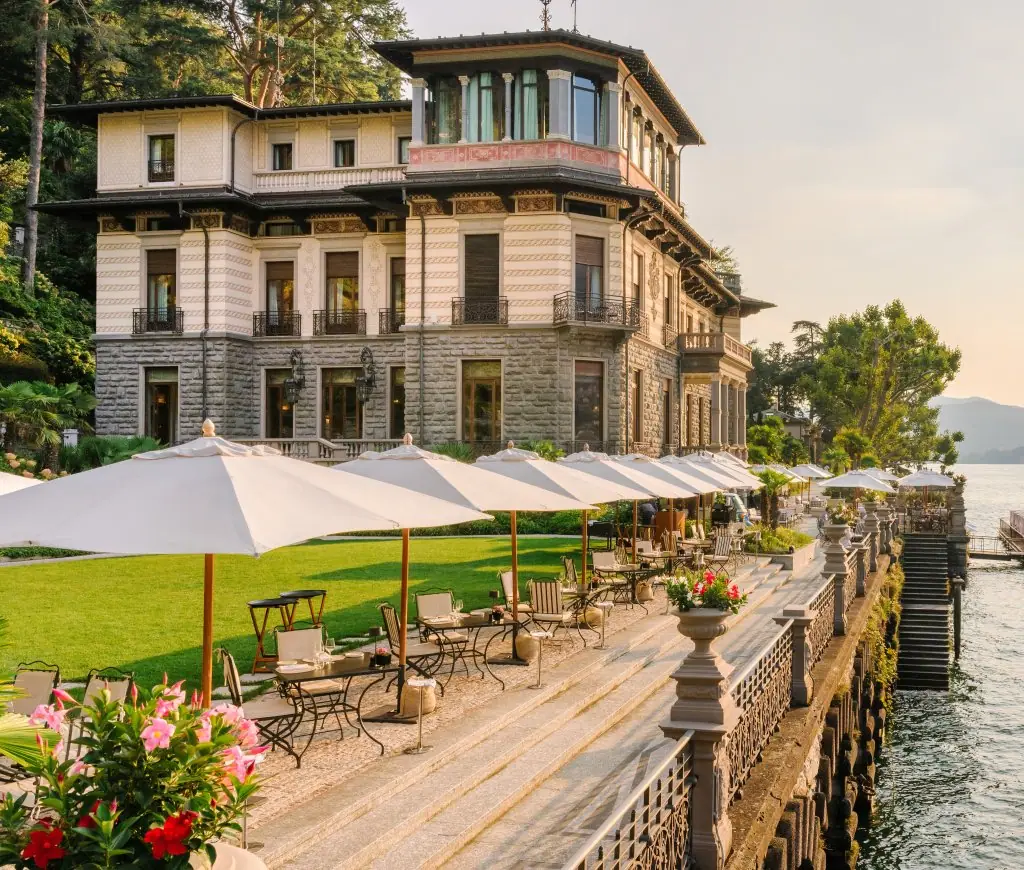A nineteenth century villa on a lakeshore with white umbrellas on the lawn in front