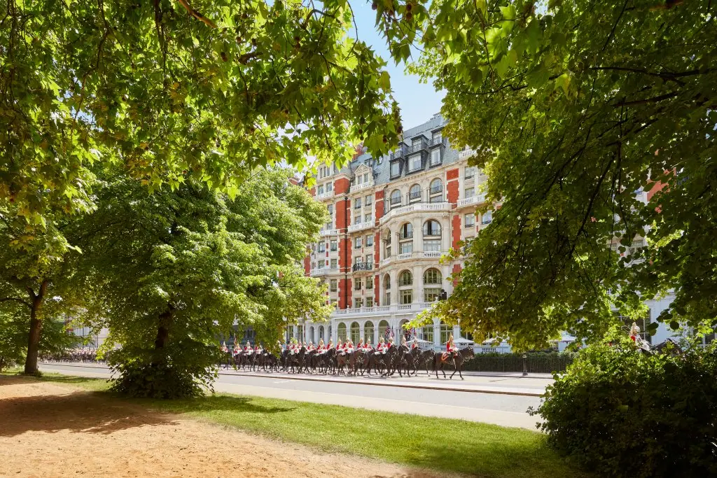 A red brick and stone Victorian hotel facade seen through trees in a park