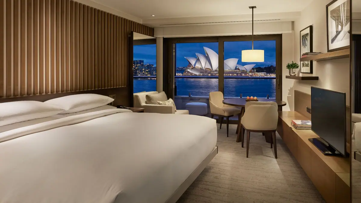 A bedroom with a wall of glass looking directly at an opera house across a harbour