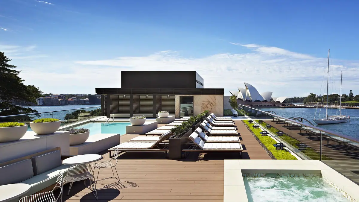 A rooftop pool and loungers with a white shelled opera house across the water