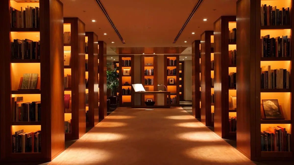 A long room lined with lit timber bookshelves and a pale floor