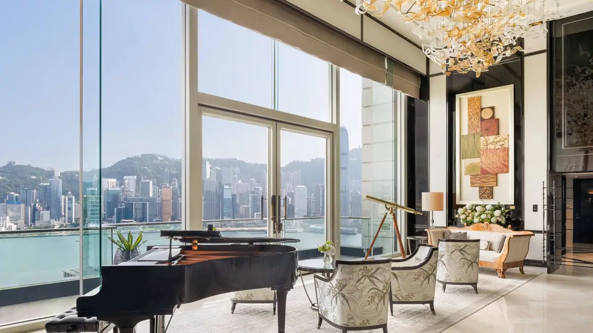 A suite sitting room with a grand piano and a wall of glass over a harbour
