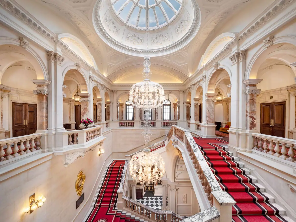 A grand stone staircase with a red carpet under a domed and painted ceiling