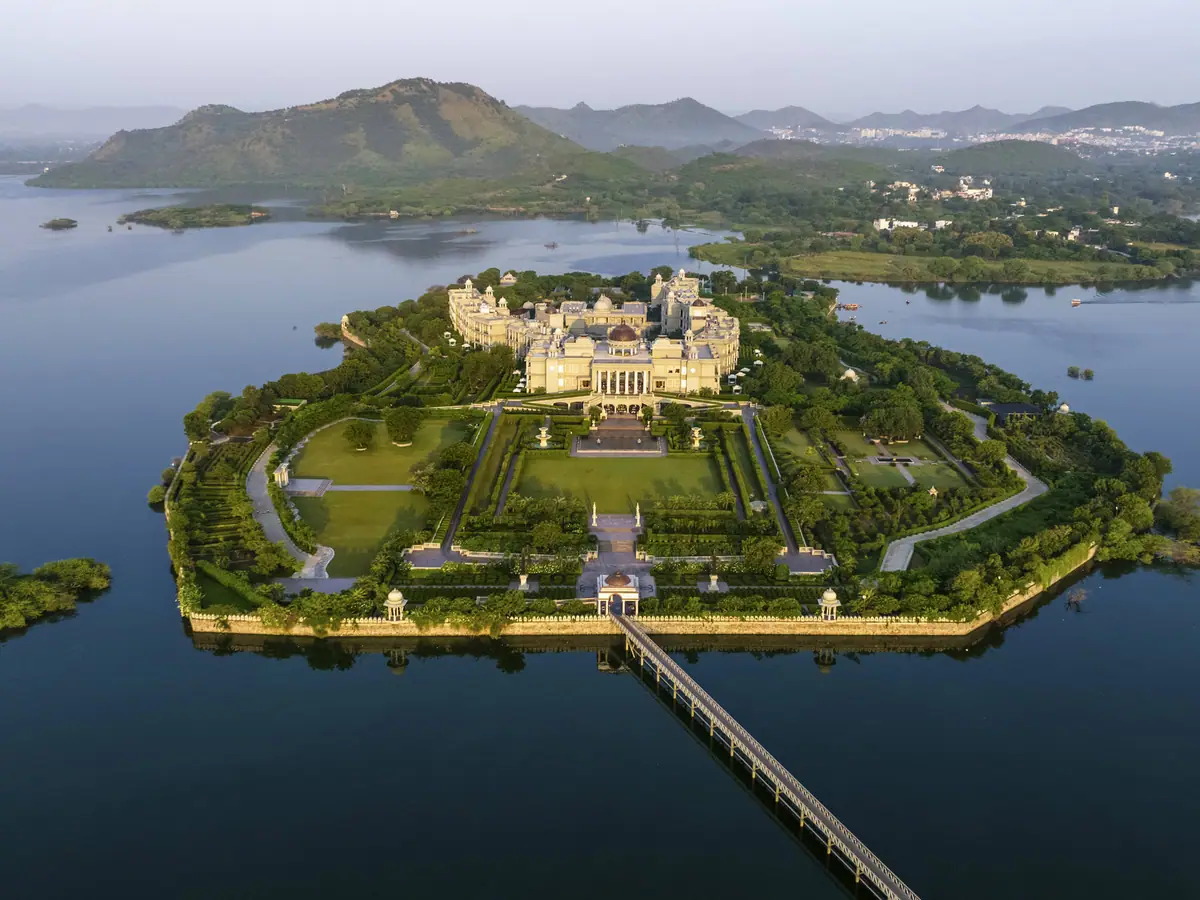 An aerial view of a palace on a wooded island in a lake ringed by hills