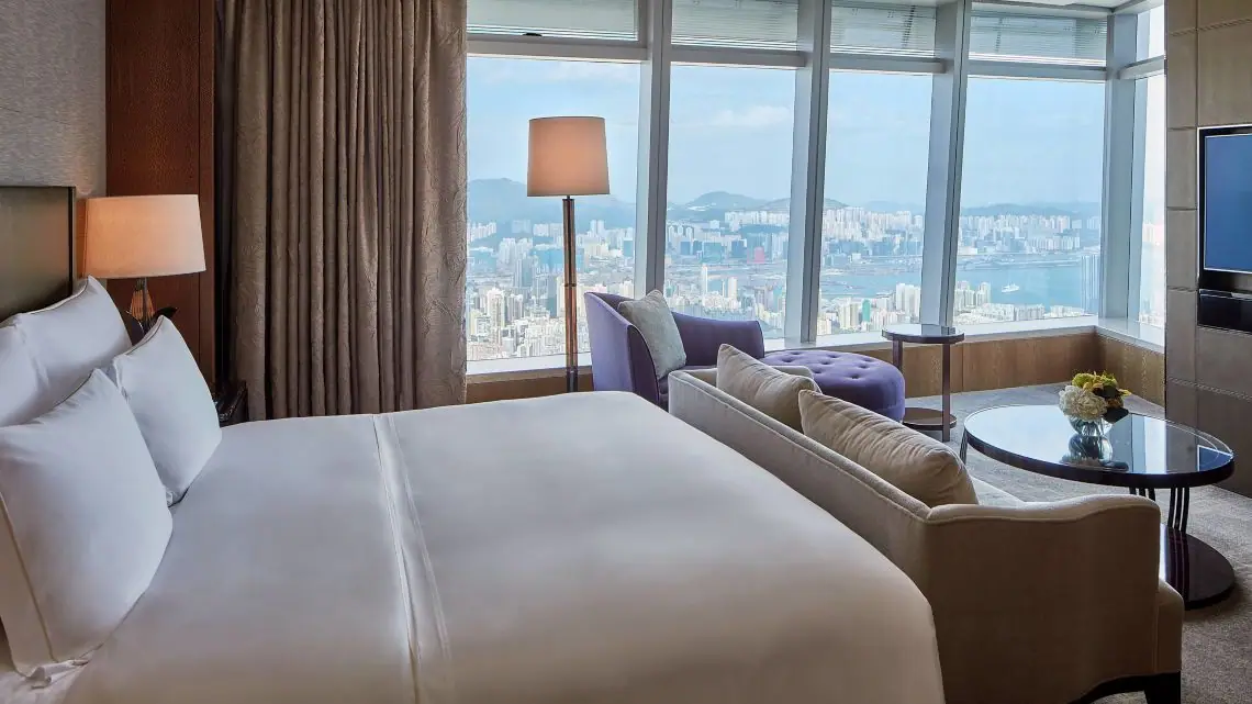 A bedroom with a sofa and a corner of glass looking down on a harbour