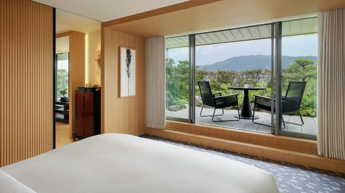 A bedroom opening onto a terrace above a river and wooded hills