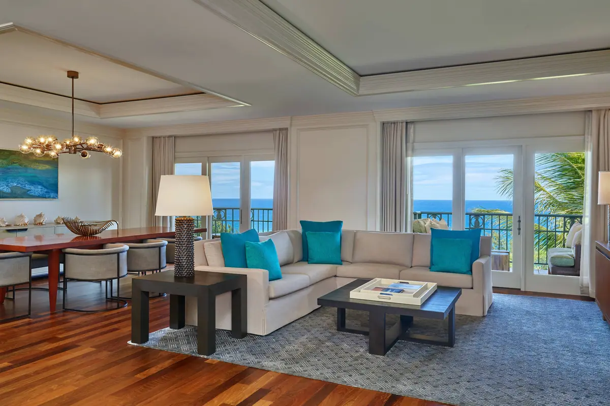 A suite sitting room with pale sofas and doors open to palms and the sea