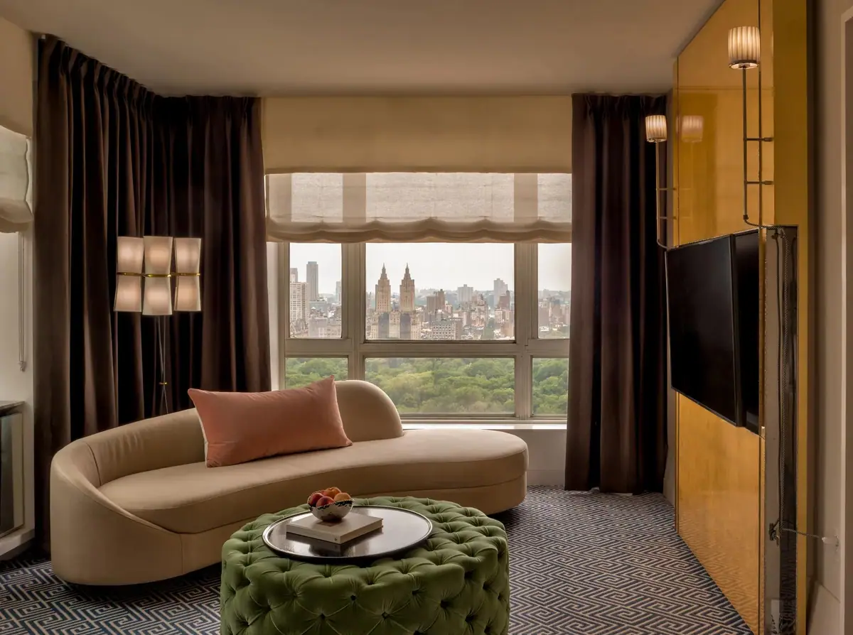 A bedroom with a curved sofa and tall windows onto a park