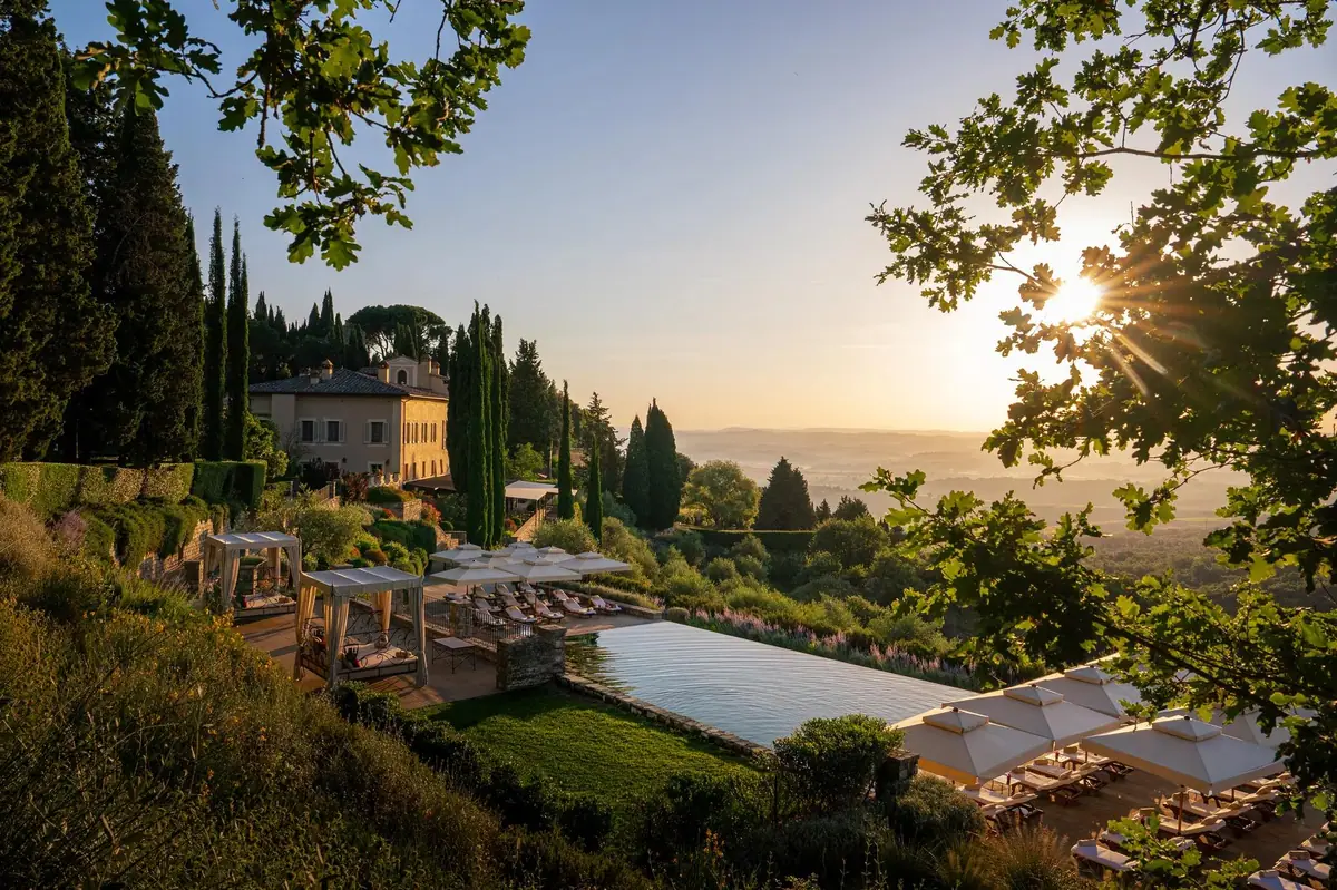 A pool and cypress trees above rolling hills at sunrise