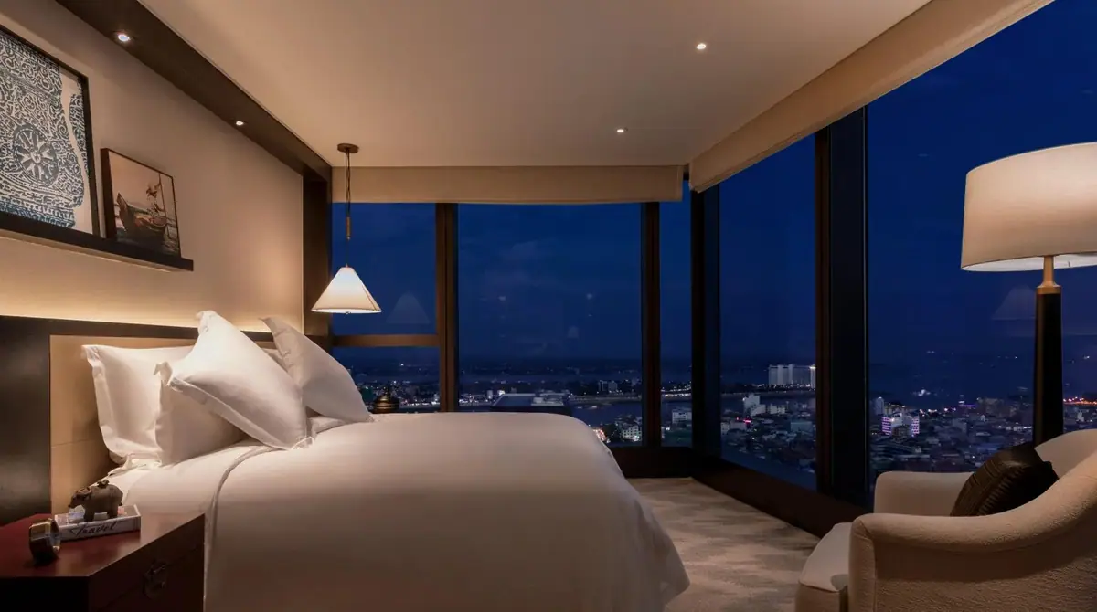 A bedroom with dark timber and a wall of glass over a city at night