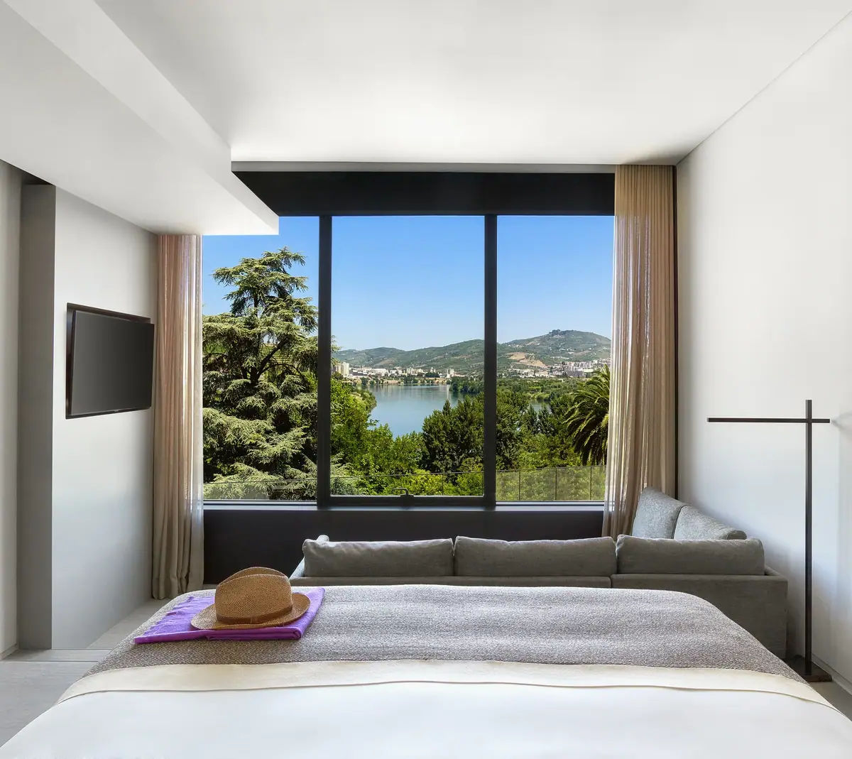 A bedroom with a wall of glass looking over terraced vineyards and a river