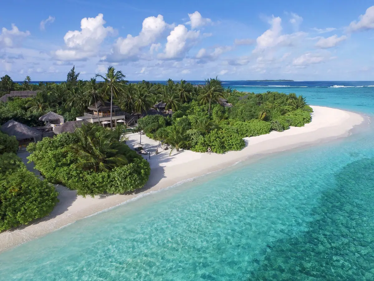 An aerial view of a green island with a white beach and a pale blue lagoon