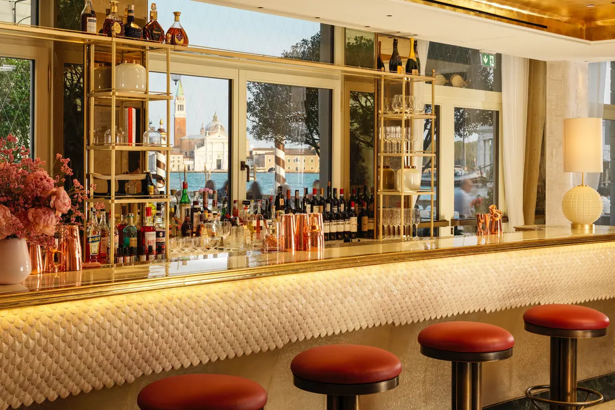 A bar counter with red topped stools and tall windows onto a canal