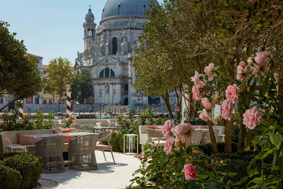 A garden of pink roses and clipped hedges with a domed church across the water behind