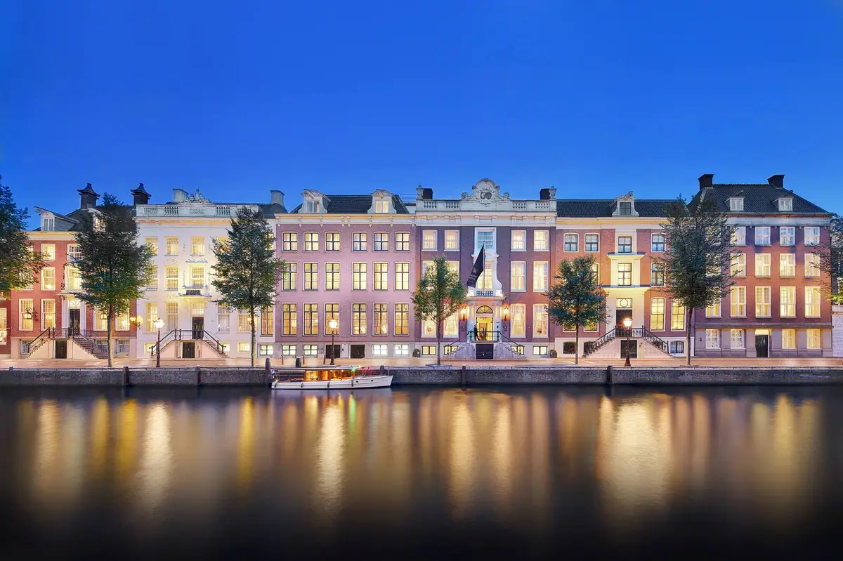 A row of tall seventeenth century canal houses lit from inside at dusk