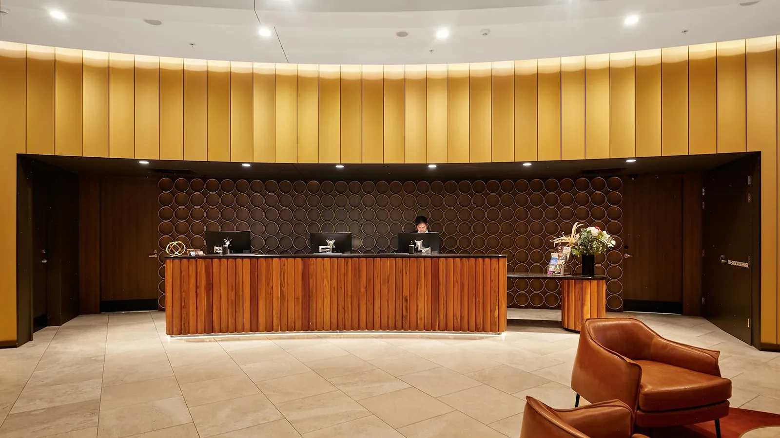A long timber reception desk under a curved brass wall, with leather armchairs to one side
