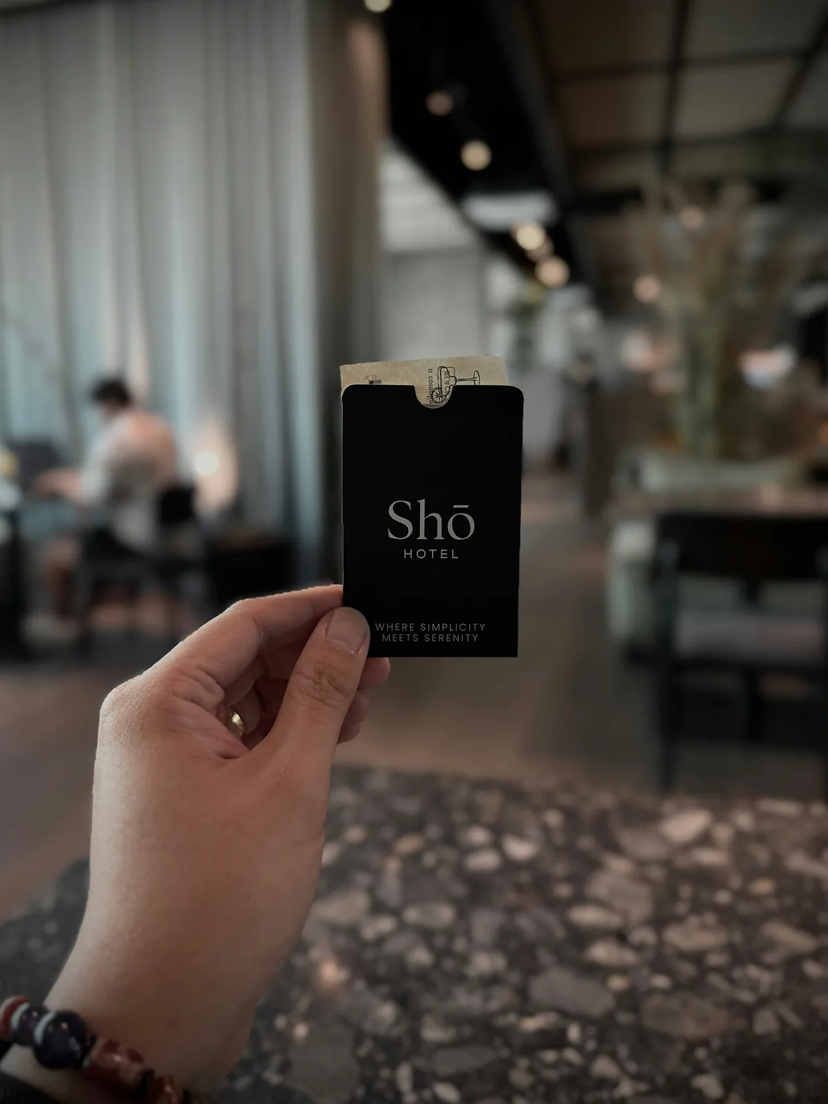 A hand holding a black hotel key card in a quiet ground floor lounge