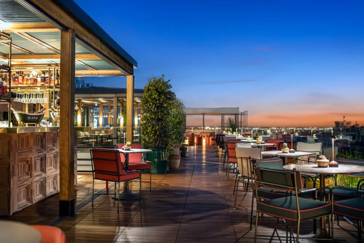 The covered rooftop restaurant at Bless Hotel Madrid at dusk with red chairs and city lights