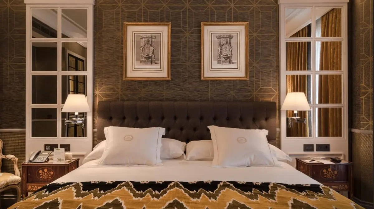 A guest room at Heritage Madrid with a brown tufted headboard and framed prints
