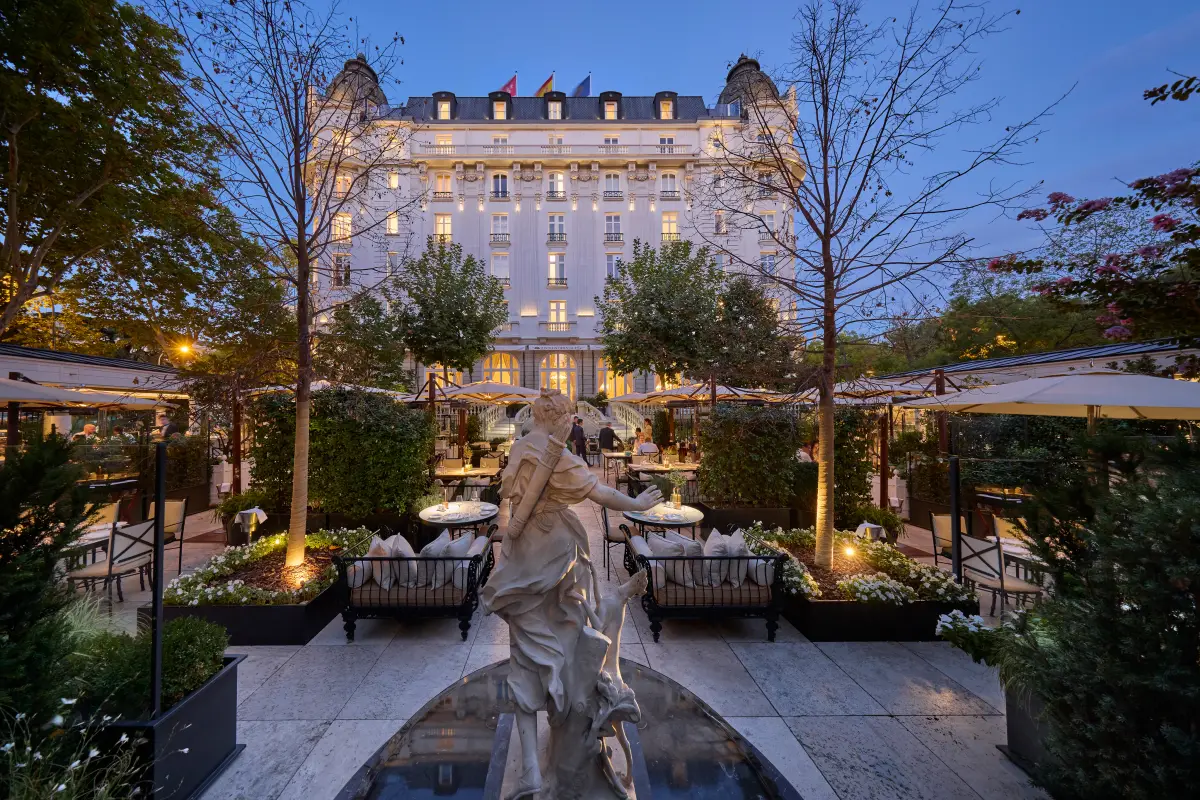 The Belle Epoque facade of the Mandarin Oriental Ritz Madrid lit at dusk above its garden