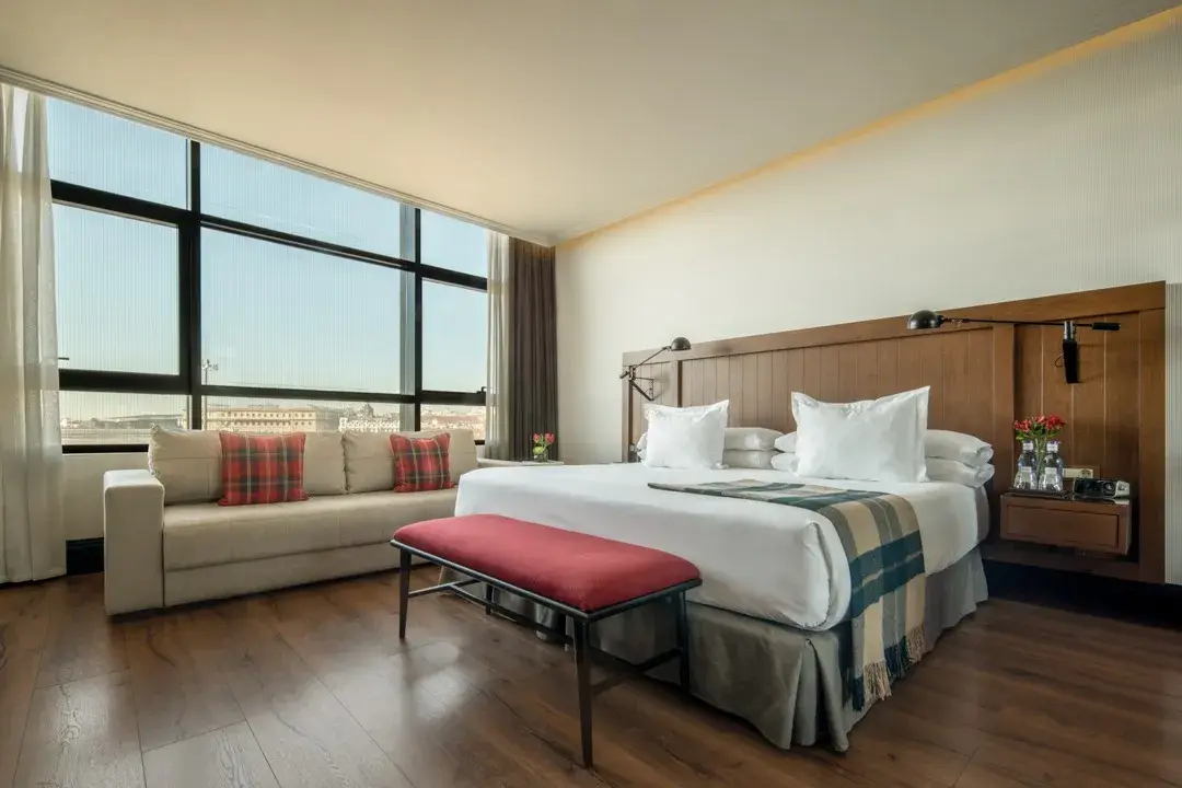 A junior suite at Only YOU Hotel Atocha with a corner window, a sofa and a red bench at the foot of the bed