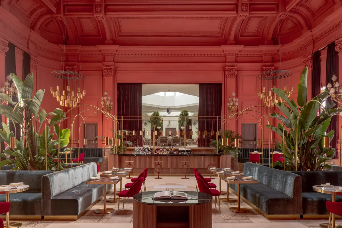 A dining room at Gran Melia Palacio de los Duques with coral walls, gold trim and velvet seating