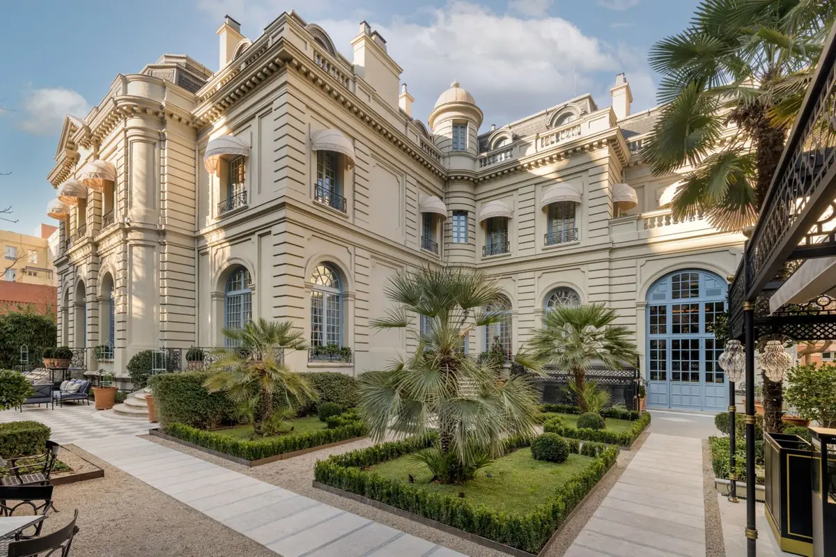 The white palace facade of Santo Mauro behind palms and clipped hedges