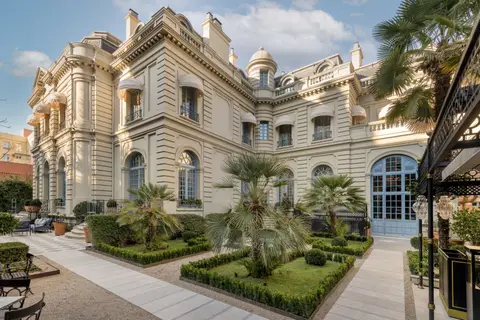 The white palace facade of Santo Mauro behind palms and clipped hedges