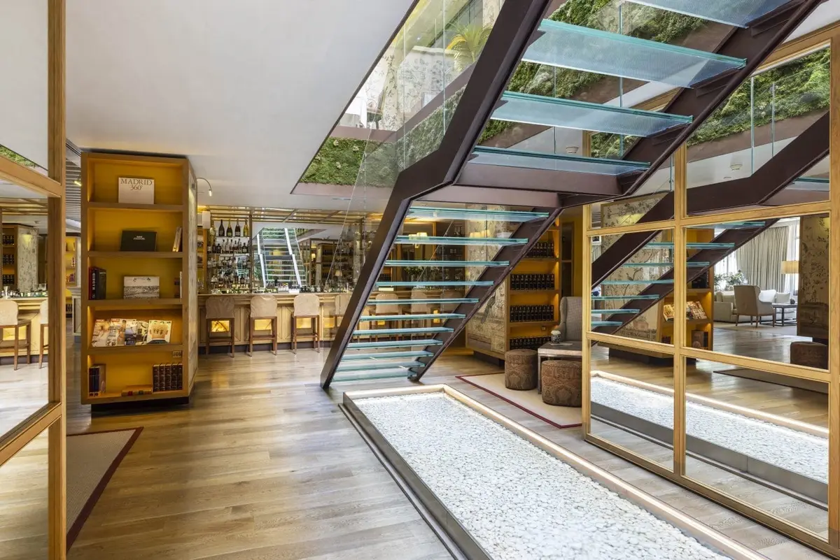 The glass and timber staircase at URSO Hotel and Spa descending beside a gravel courtyard