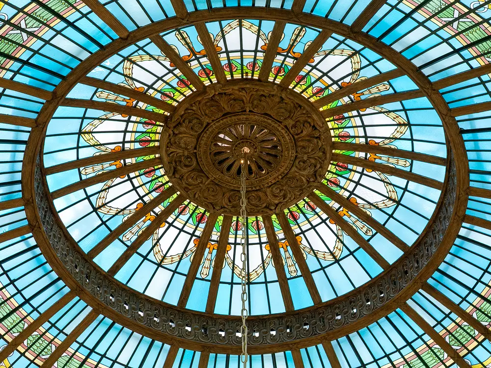 The stained glass and iron dome above the rotunda at The Palace Madrid seen from below