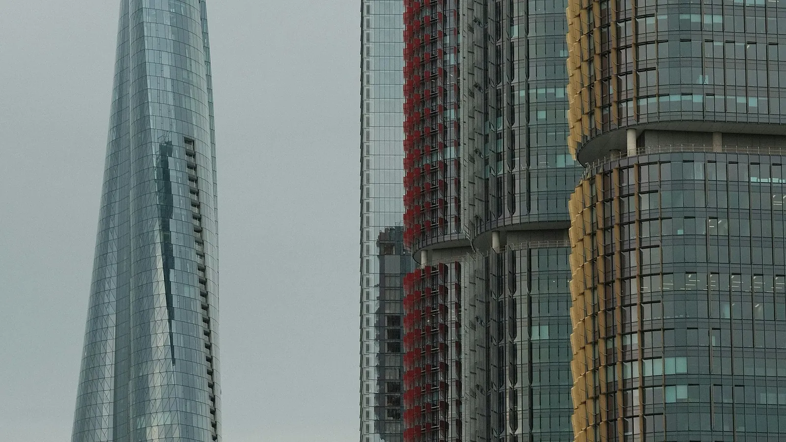 A slim glass tower rising among newer high rise buildings on a pale city skyline