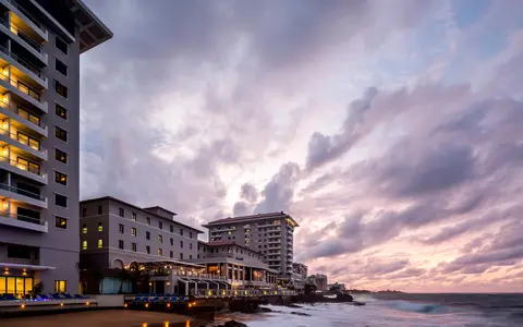 The Condado Vanderbilt seen from the water at dusk with the modern towers behind the 1919 building