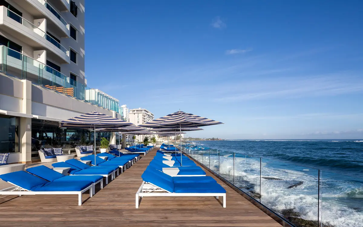 Row of blue loungers on a narrow pool terrace above the rocks and surf