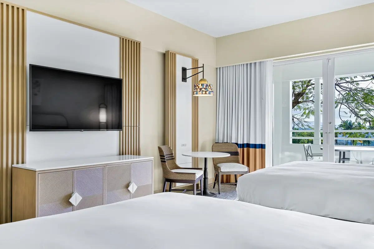 Two queen beds, a small dining table and a wall mounted television in a garden view room