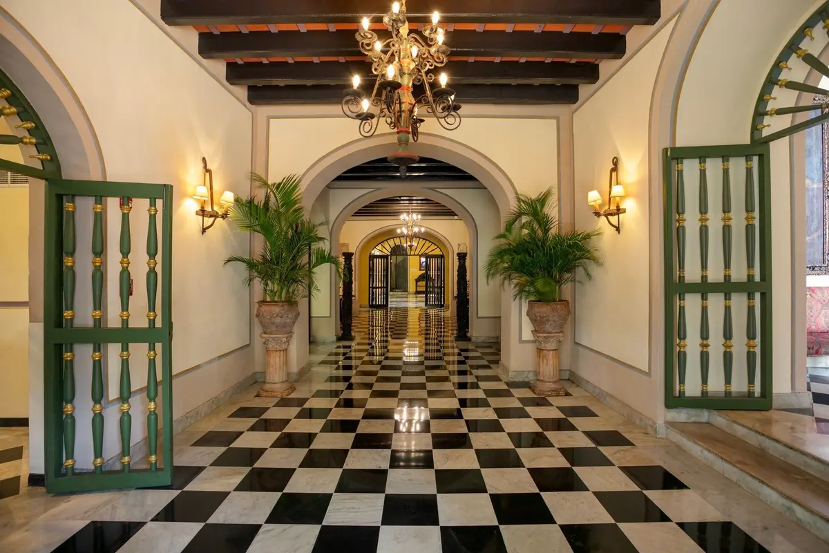 Entrance hall with a black and white chequerboard floor running between arches to a lit doorway