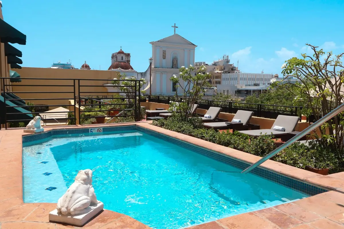 Small rooftop plunge pool and loungers with a white church tower rising behind