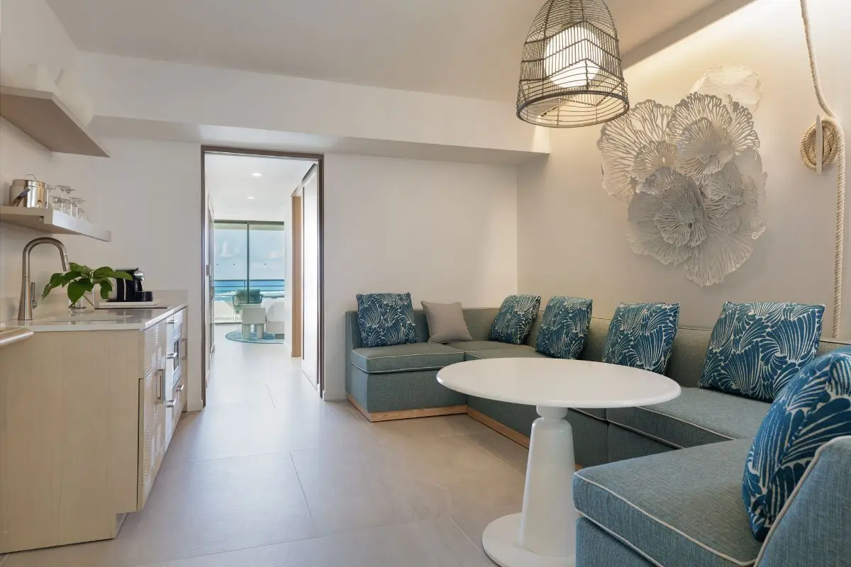 Suite living area with a pale banquette, a round table and a kitchenette facing the sea