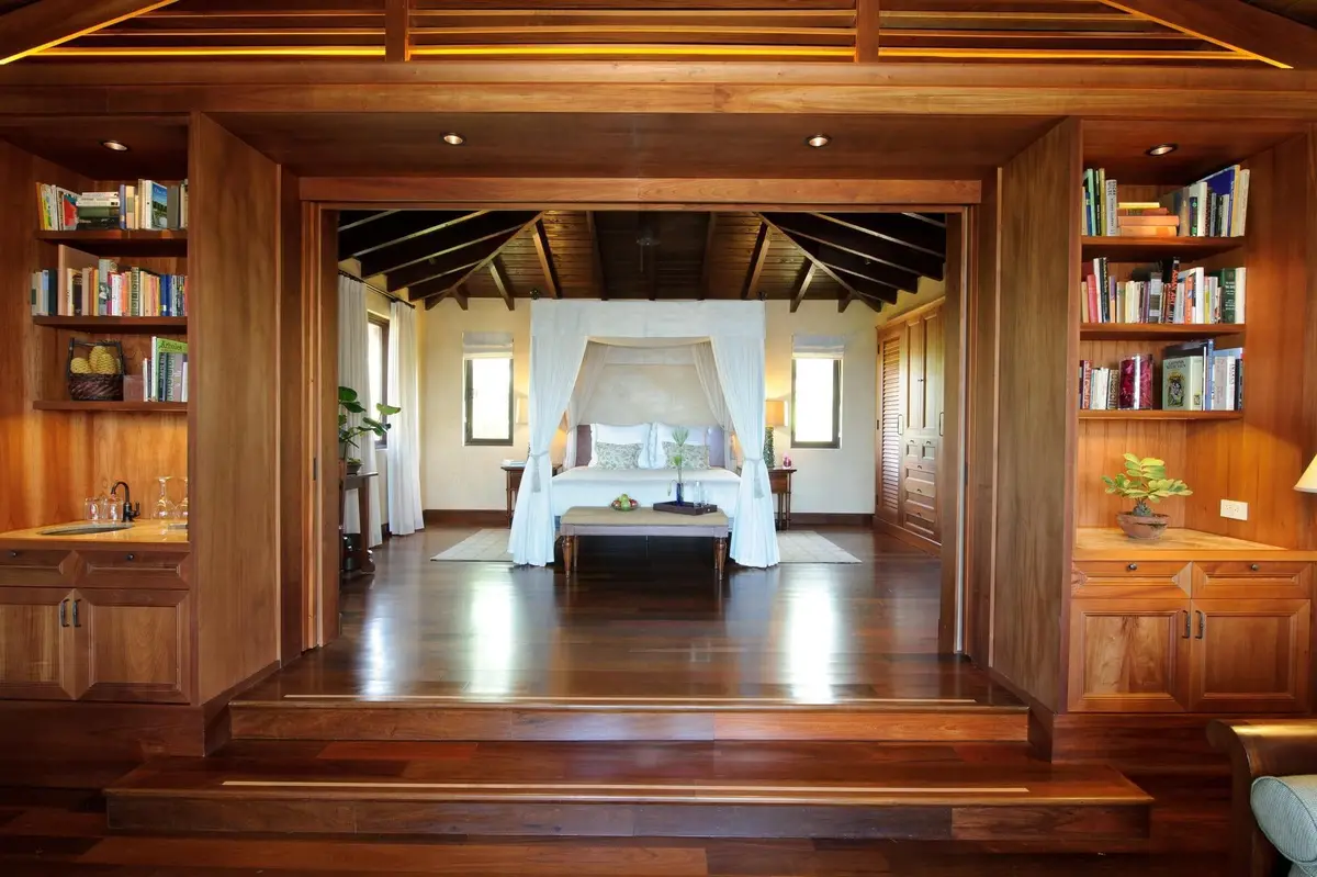 Four poster bed under a beamed ceiling with a desk and an open doorway to the sea