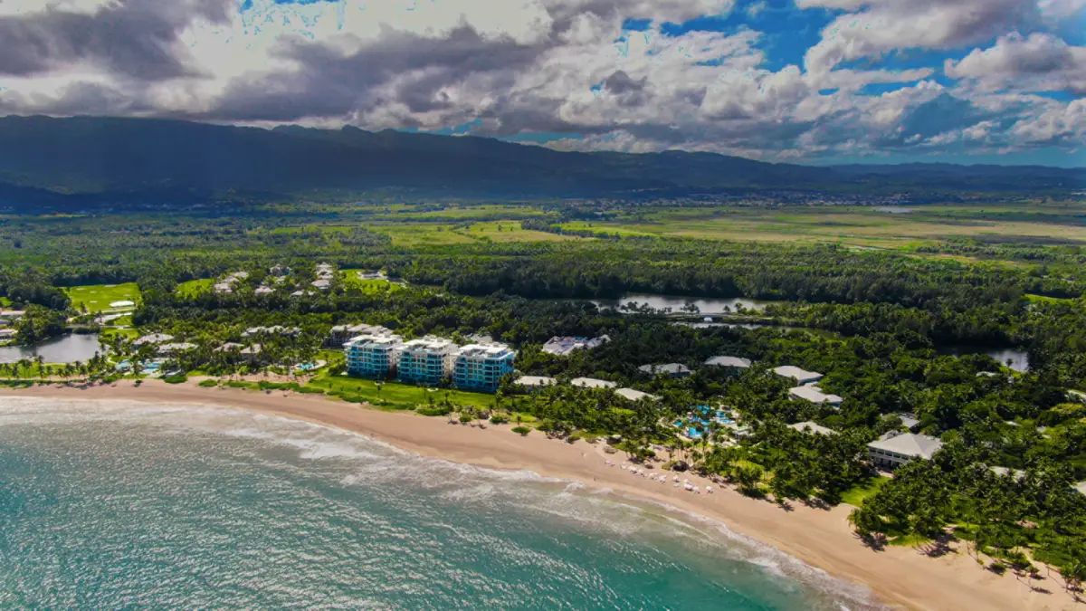 Aerial view of the resort buildings along the beach with the El Yunque mountains behind