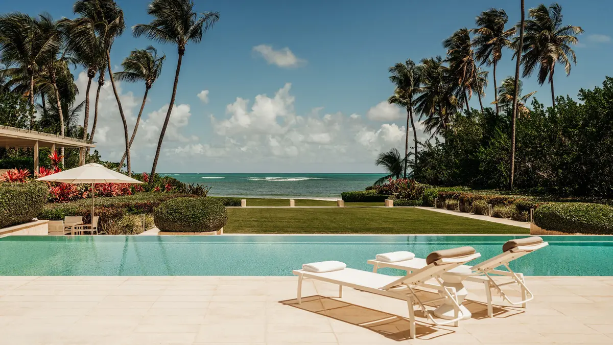 Infinity pool and white loungers on a lawn above the beach