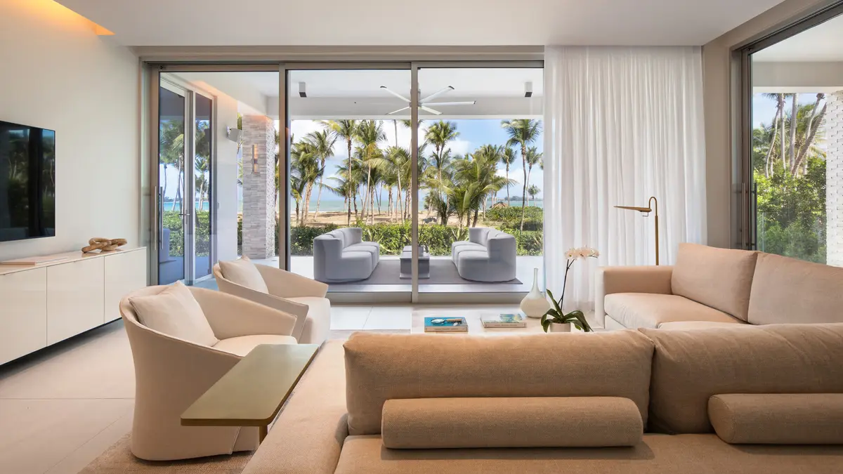 Suite living room with deep sofas opening through full height glass to a terrace and palms