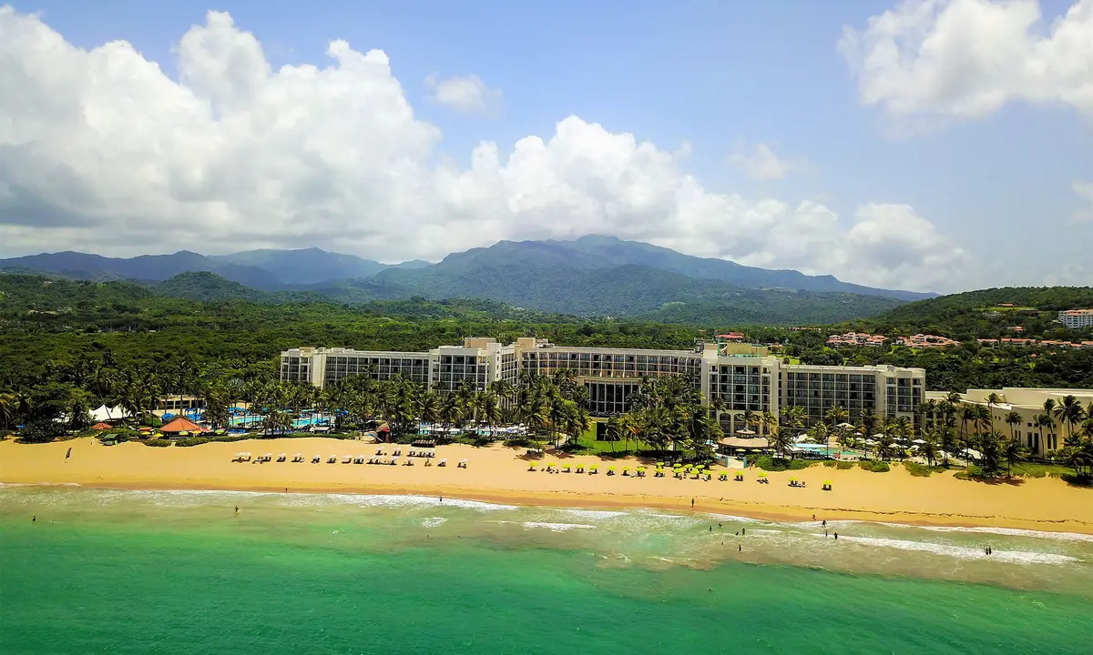 The resort stretched along a wide beach with the green ridge of El Yunque behind it
