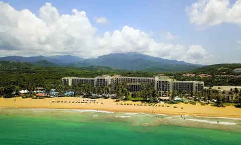 The resort stretched along a wide beach with the green ridge of El Yunque behind it