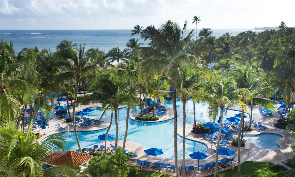 Main pool complex with blue umbrellas and palm islands seen from the air