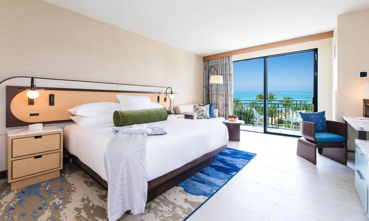 Guest room with a curved headboard and sliding doors onto a balcony above the palms