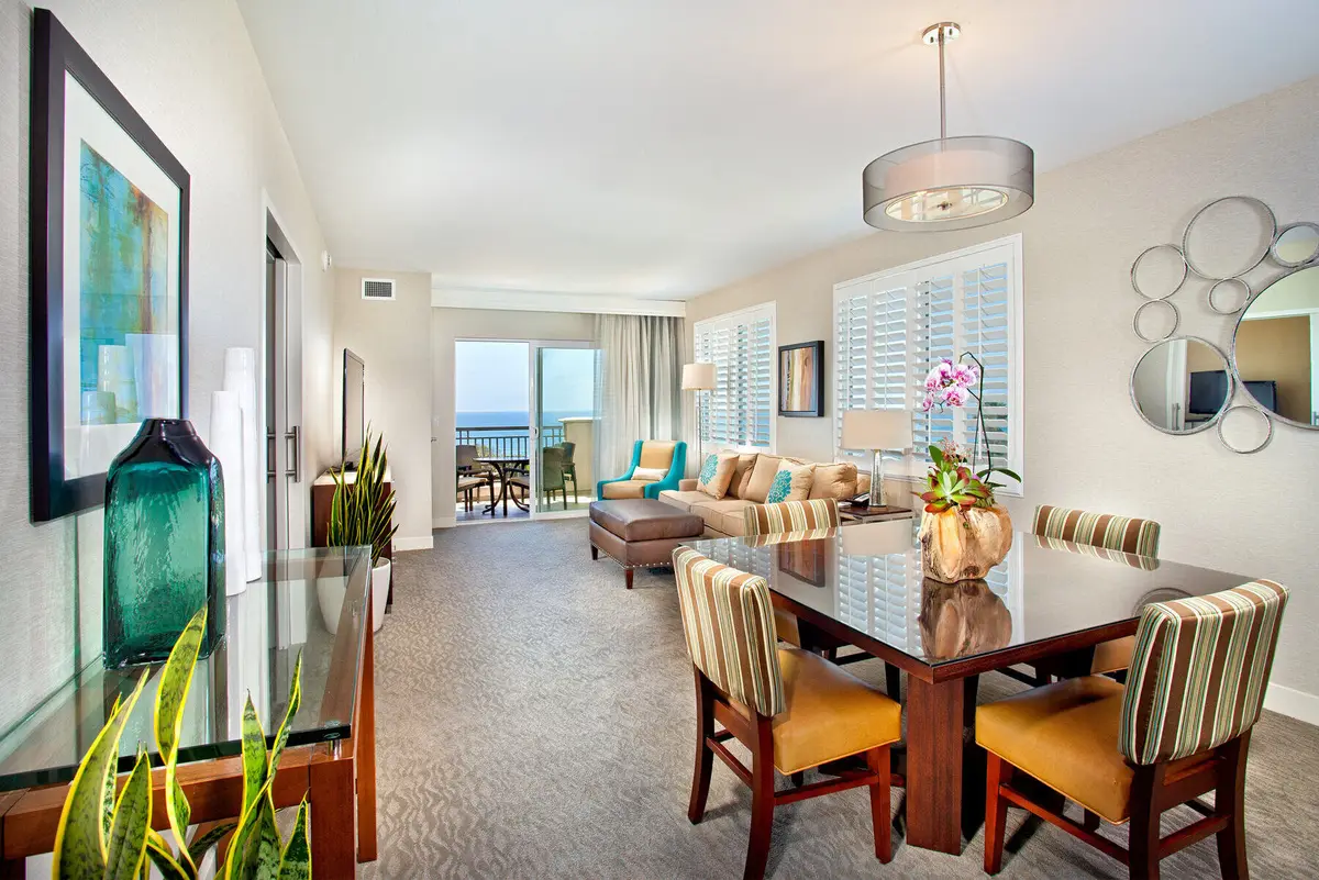 A suite with a dining table, sofa and shuttered windows looking out to the sea