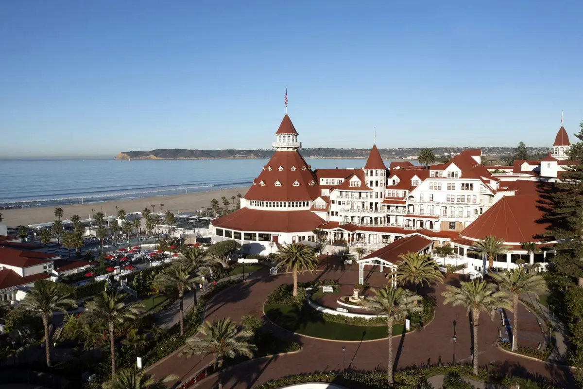 The red turrets and white timber of Hotel del Coronado seen from the air above the beach