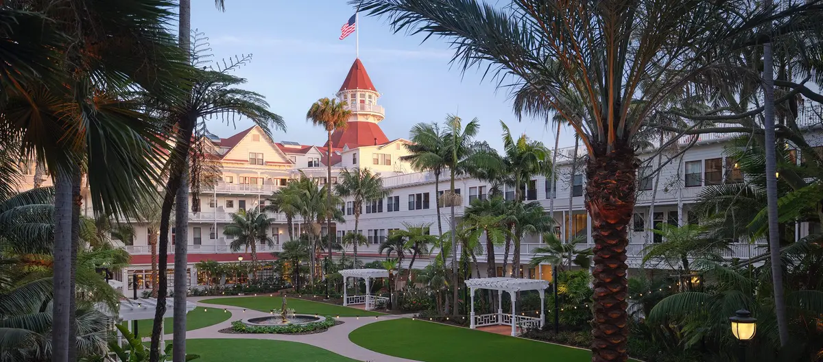 The garden courtyard at Hotel del Coronado with lawns, palms and the red turret behind