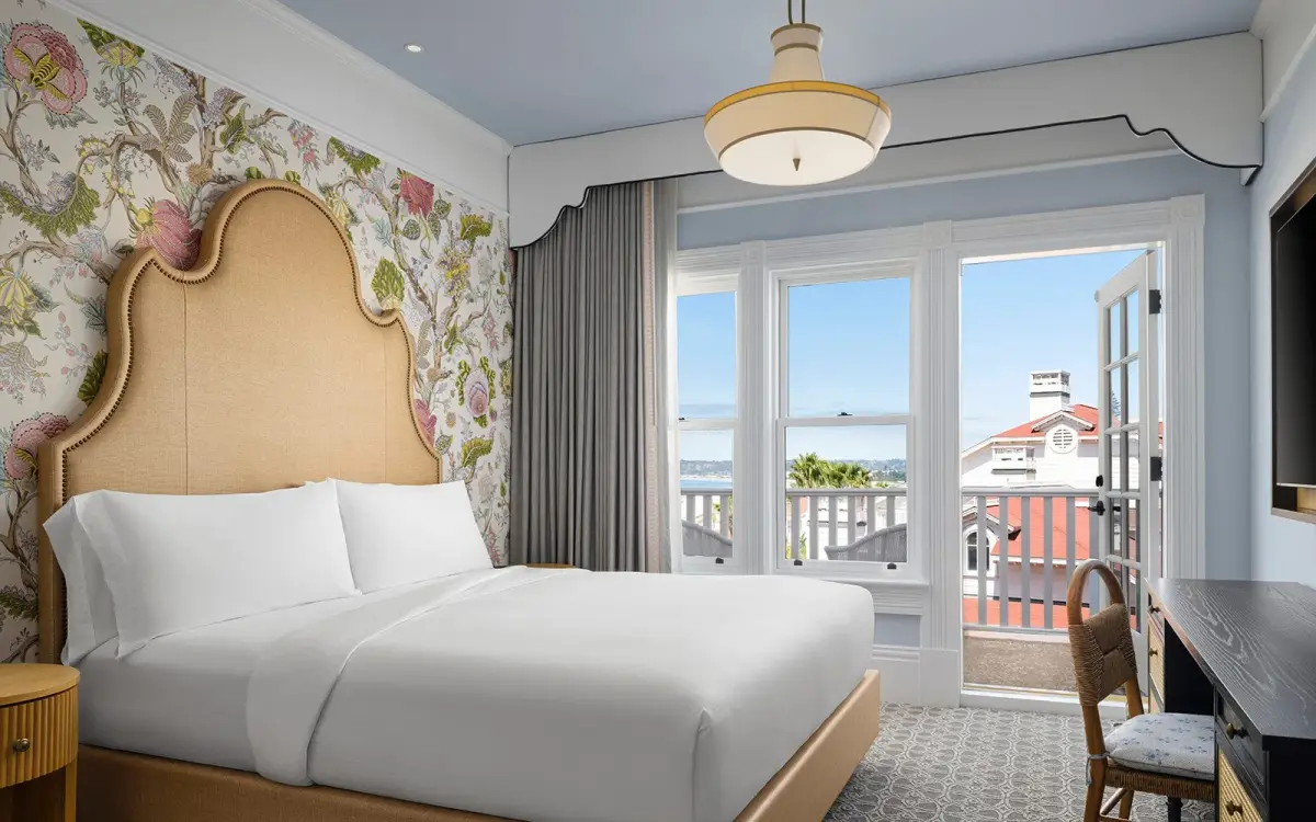 A king room in the Victorian building with a tall upholstered headboard, floral wallpaper and windows onto the sea