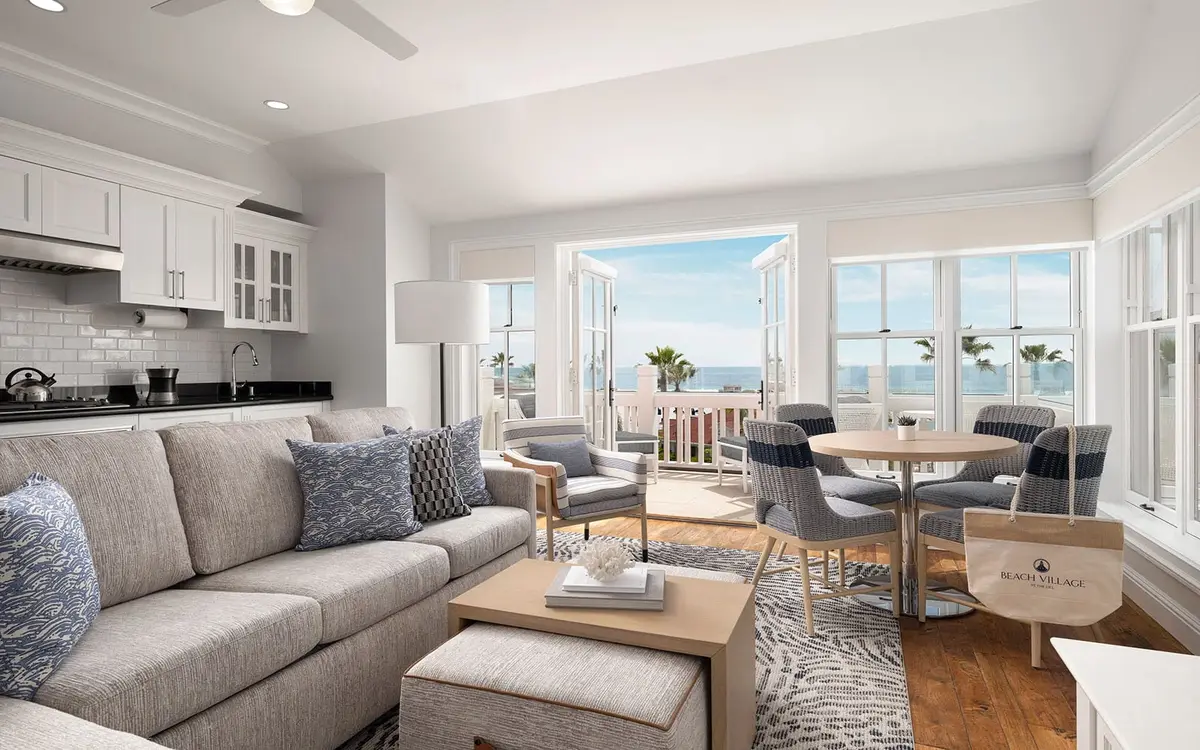 An open plan villa living room with a pale sofa, a kitchen and glass doors onto the beach